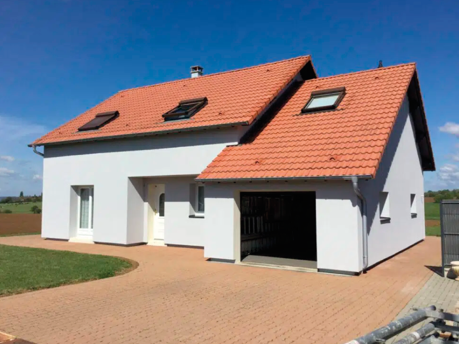 Maison moderne rénovée avec une façade blanche et un toit en tuiles rouges, située dans un environnement rural.